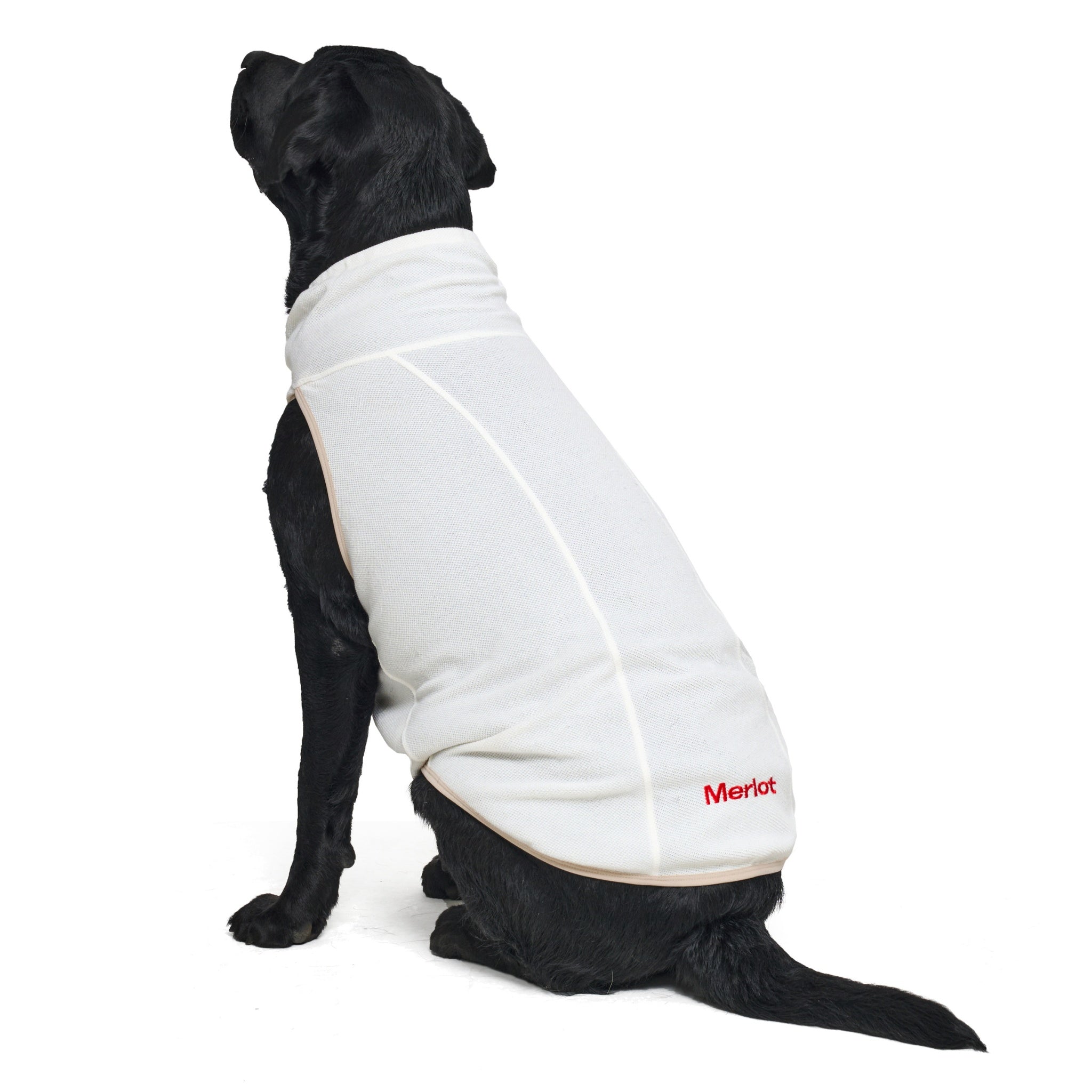 Rear three-quarter view of a black Labrador sitting down, showcasing the clean side panel seams, contrast edge trim, and red embroidered Merlot logo on the ivory dog vest.