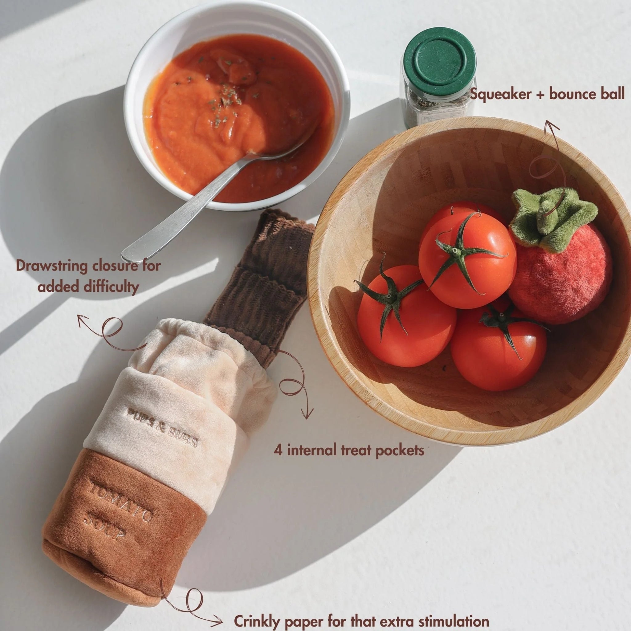 Product diagram showing the Tomato Soup nosework toy alongside real tomatoes and a bowl of soup, highlighting details like the drawstring closure, four internal treat pockets, crinkle paper, and a squeaker bounce ball.