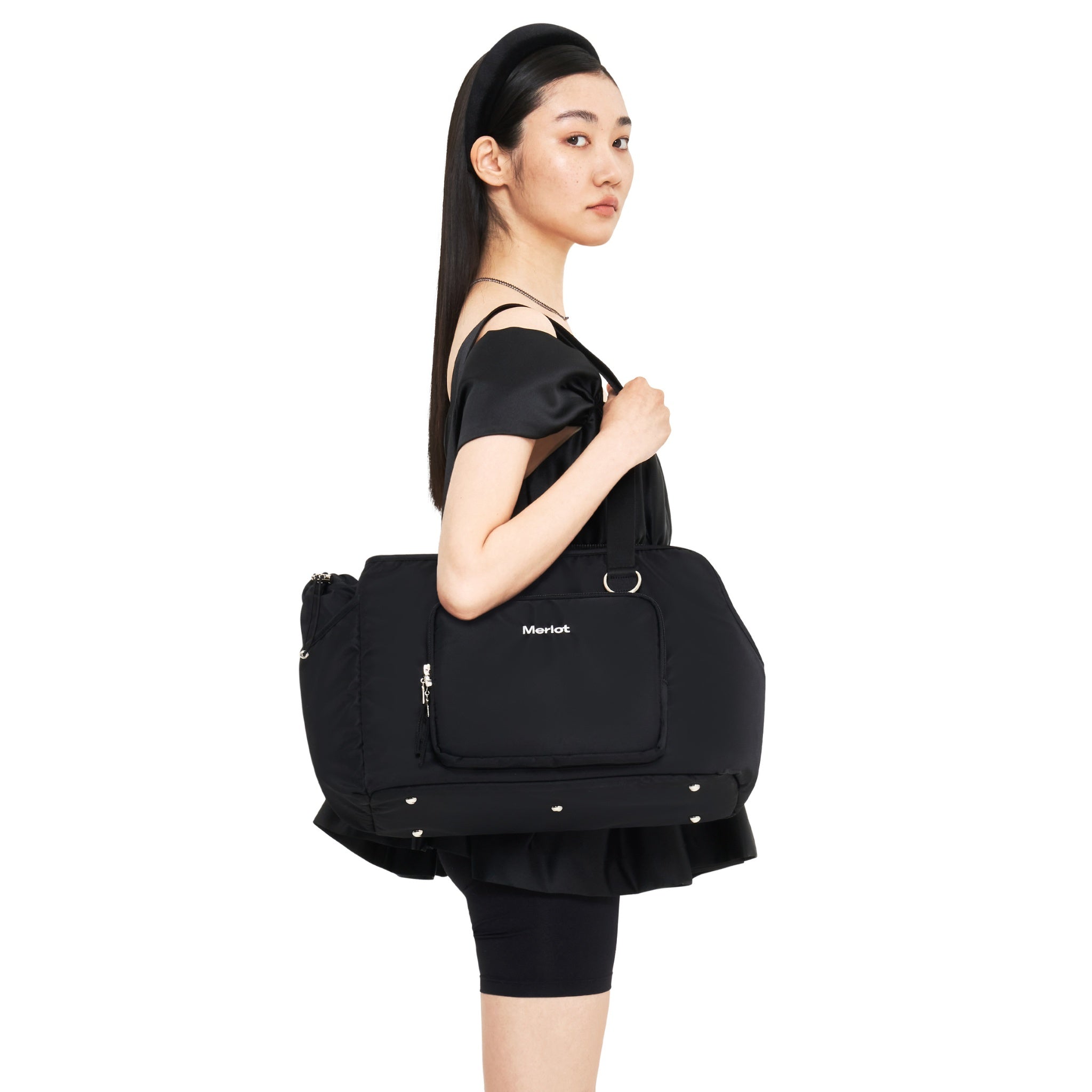 Side profile view of a model carrying the sleek black Merlot Mermer pet carrier bag tucked under her arm as a shoulder tote.