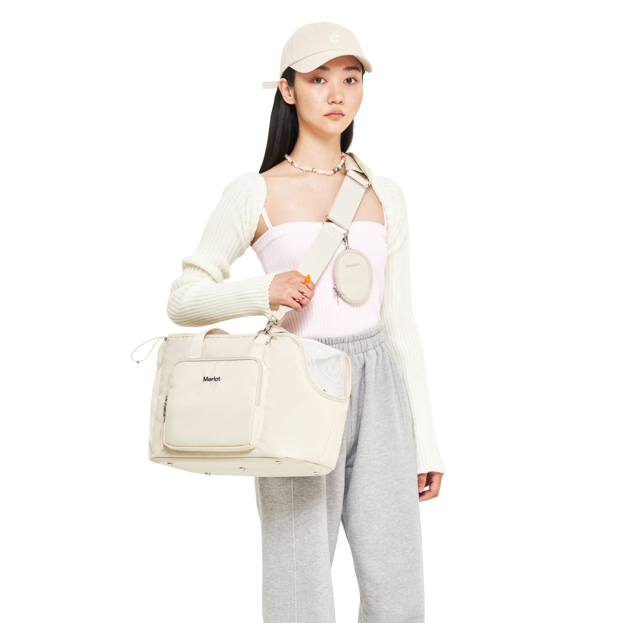 A studio lifestyle shot of a model wearing the lemon cream Merlot Mermer pet travel bag cross-body, styled with a wide cream woven shoulder strap and an attached matching round coin pouch accessory.