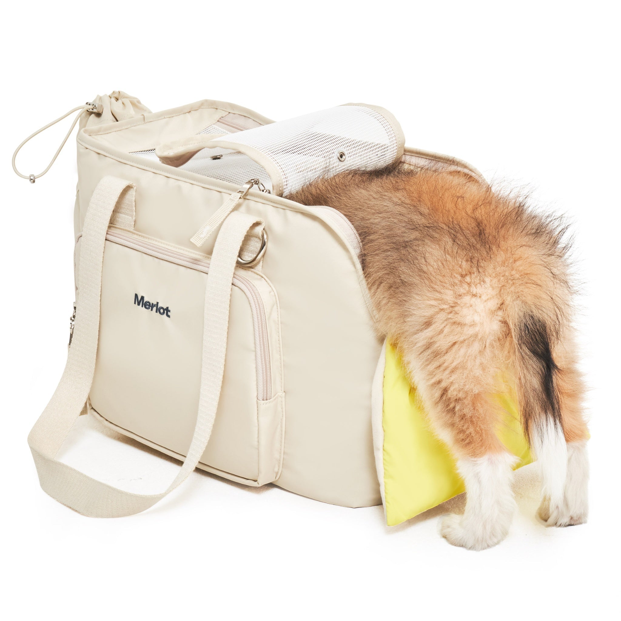 A fluffy brown puppy climbing into the open lemon cream Merlot Mermer dog carrier bag, showing the spacious side opening lined with a vibrant lemon yellow comfort cushion.