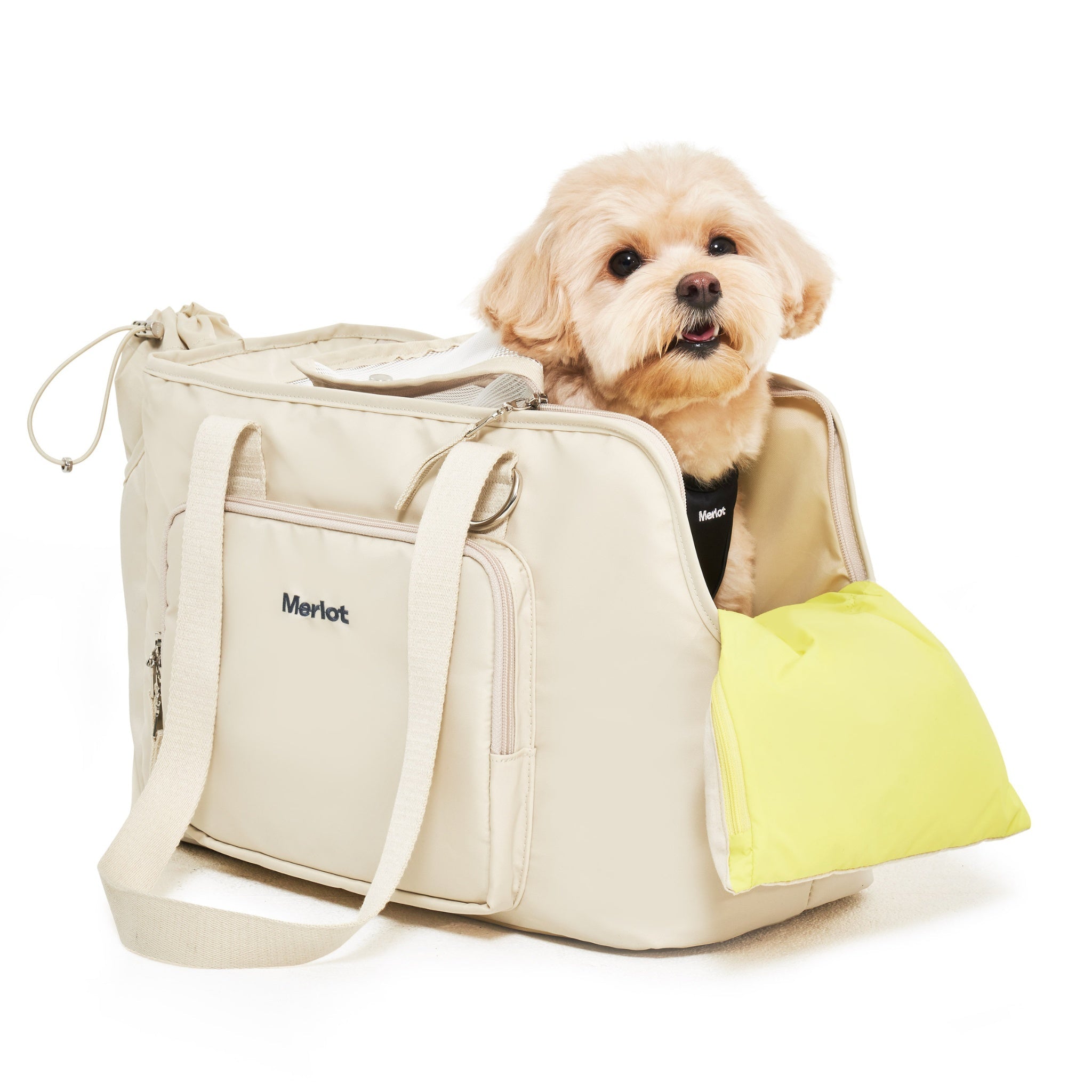 An angled three-quarter view of a small buff-colored dog looking out from the lemon cream Merlot Mermer dog carrier bag, supported comfortably by a bright yellow chin-rest cushion.