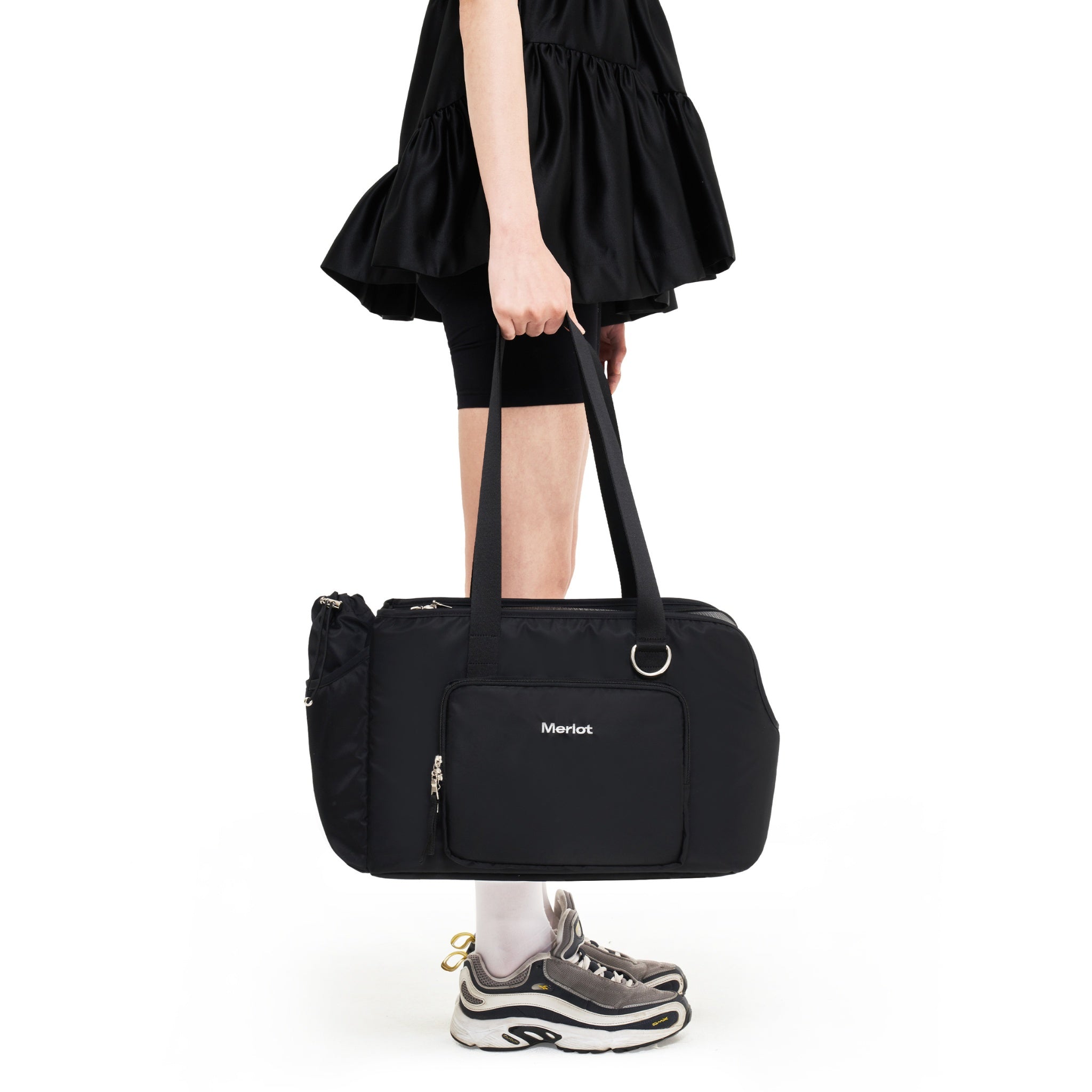 A cropped view of a model carrying the black structured Merlot Mermer dog travel bag down by her side using the integrated durable nylon web handles.