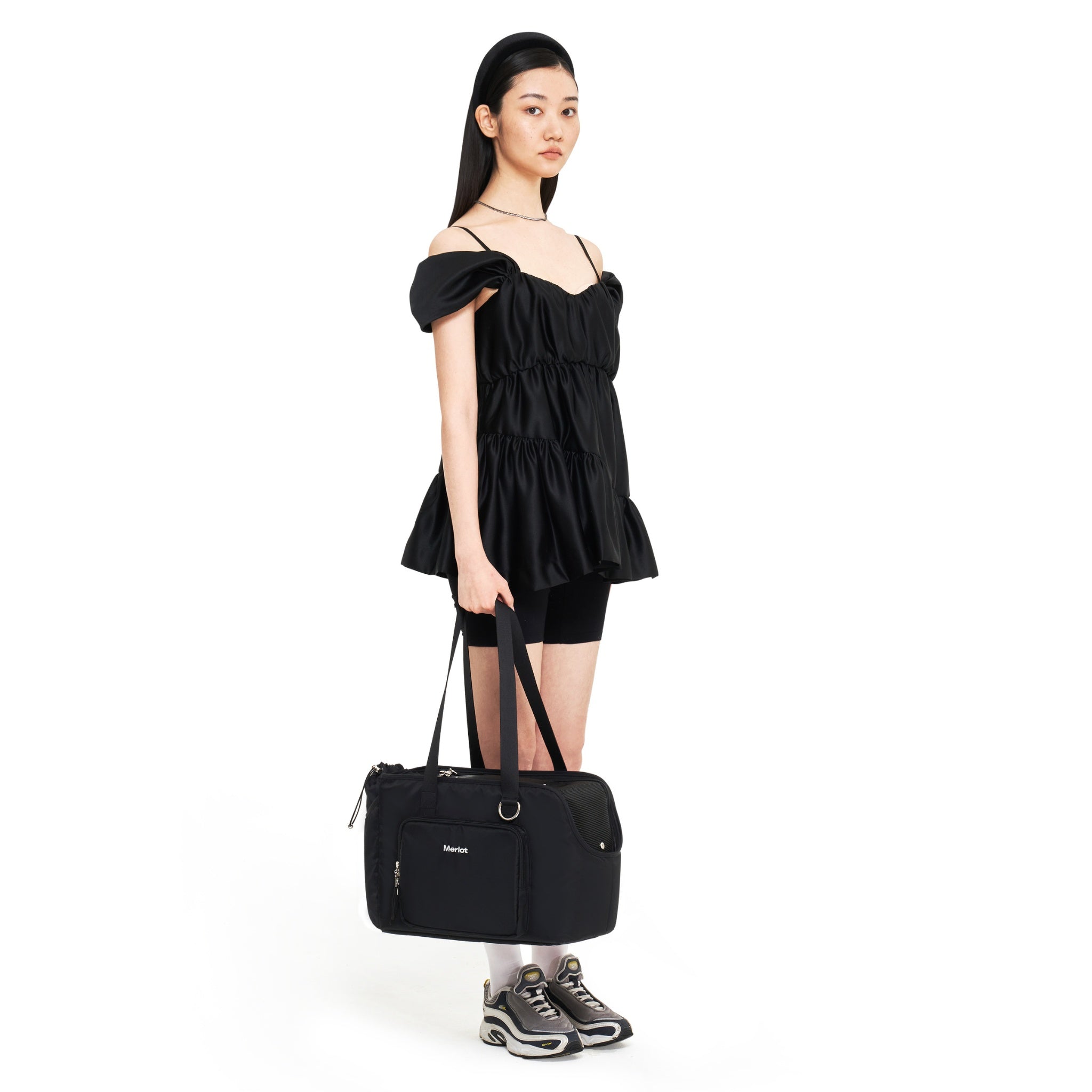 Full-body studio shot of a model holding the black Merlot Mermer pet carrier tote by its top handles, showcasing its size and transport style.