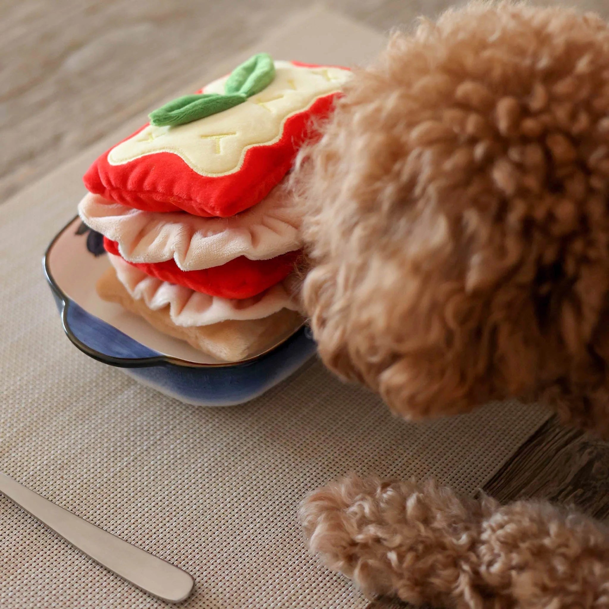 A small brown puppy sniffing a plush food-themed nosework toy to challenge its natural foraging instincts.