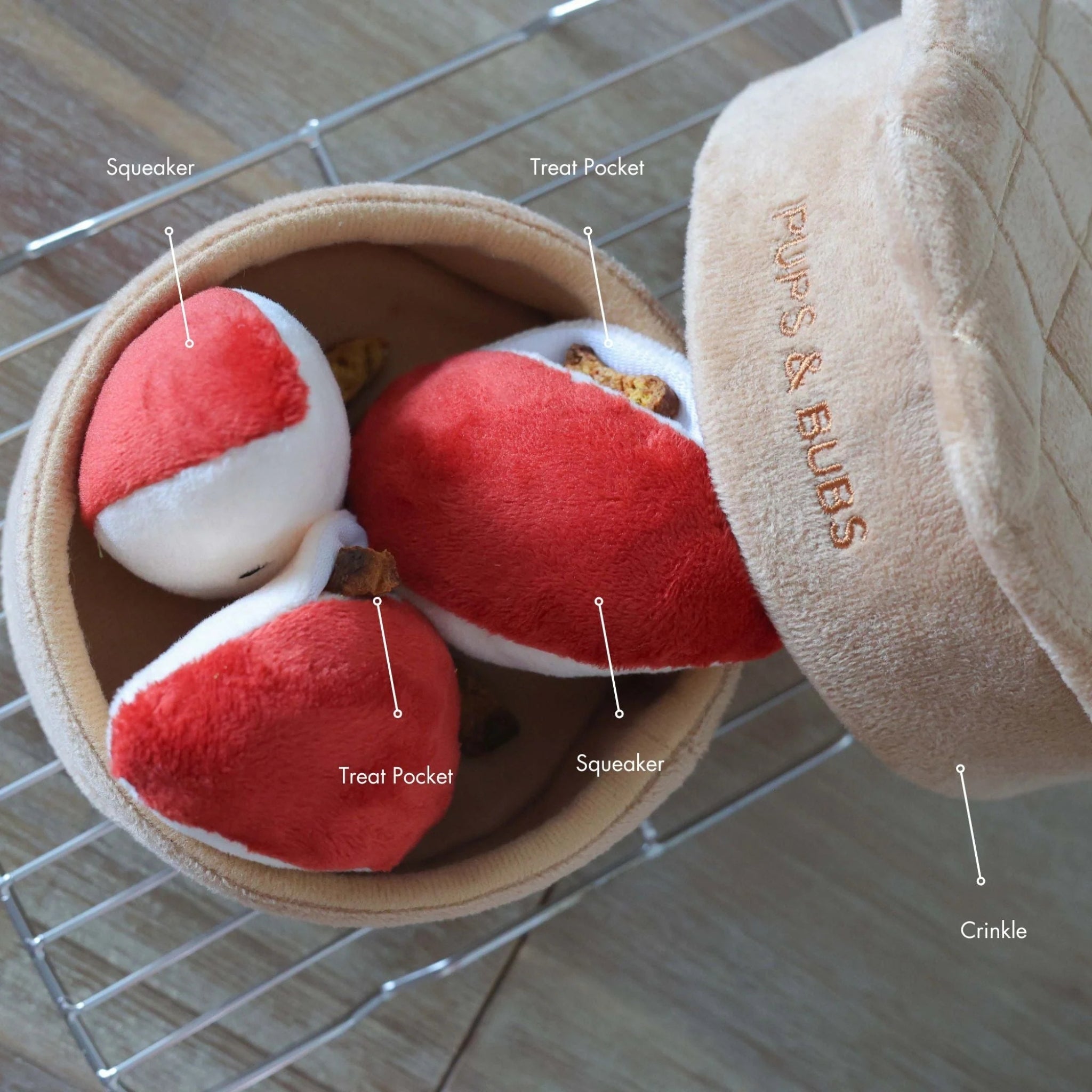 Overhead product shot of the Apple Pie puzzle dog toy by Pups and Bubs with text labels pointing out the squeaker, treat pockets, and crinkle paper features.