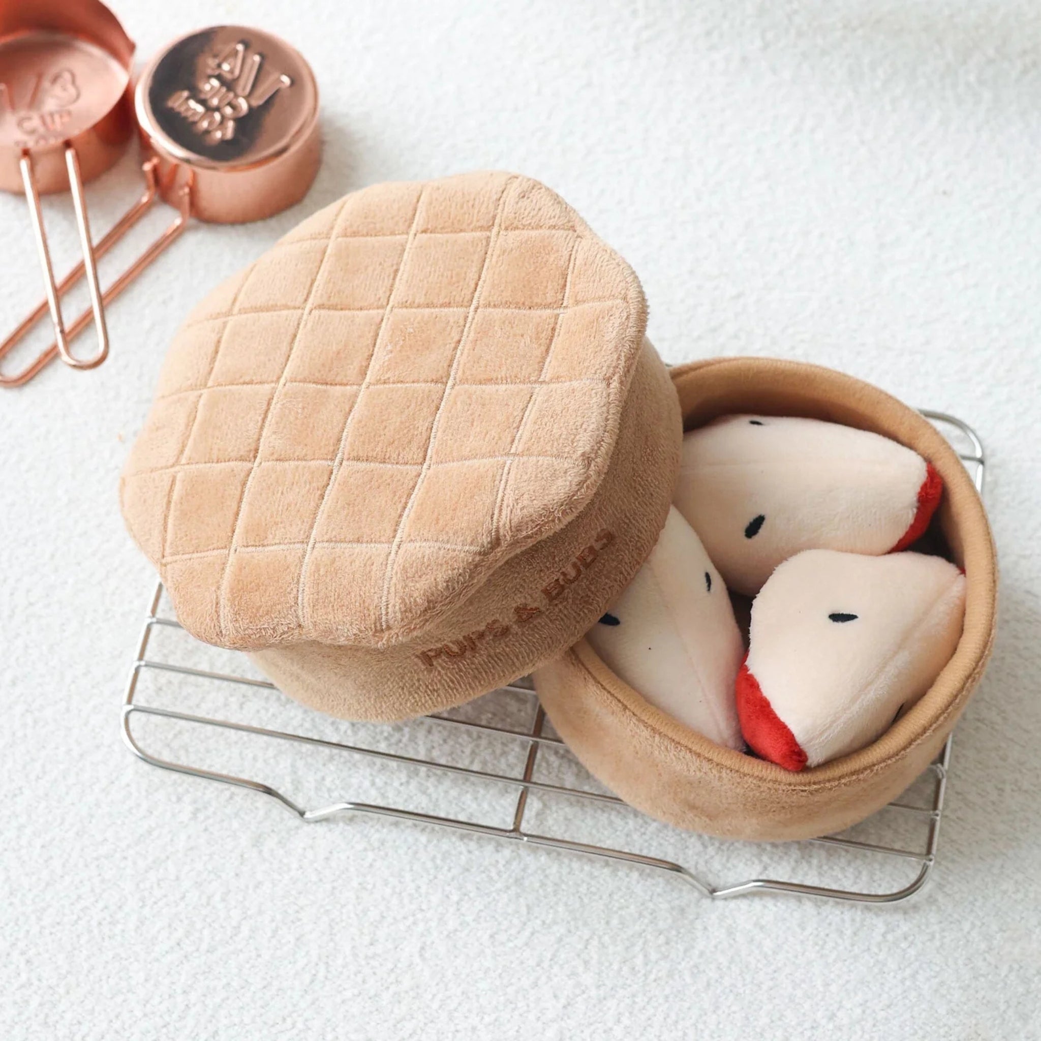 Top-down view of the soft tan lattice crust lid pushed aside to reveal multiple plush red apple slice toys inside the main pie base.