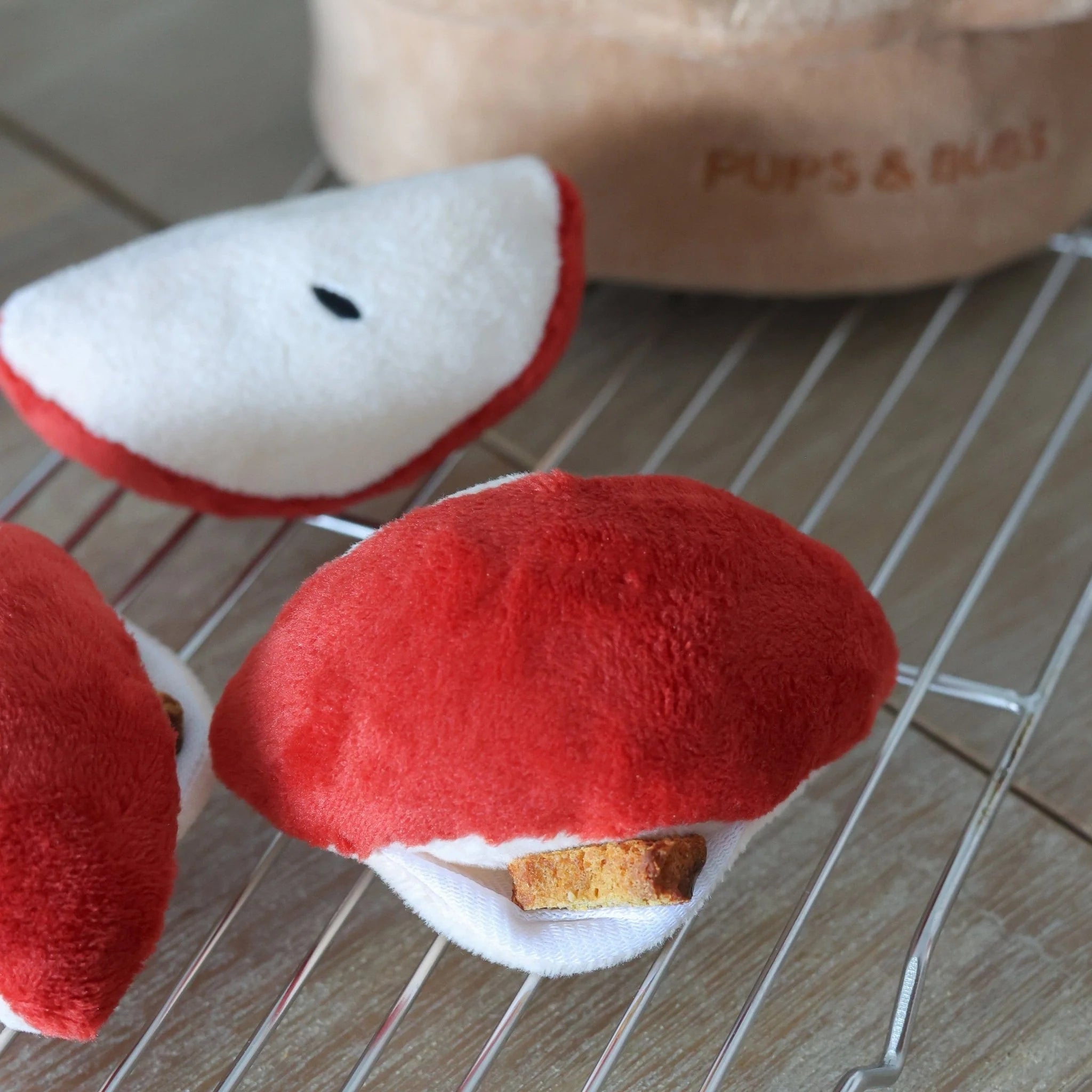 Close-up of plush red apple slices from the Pups and Bubs interactive nosework toy, showing hidden pockets stuffed with small dog treats on a cooling rack.