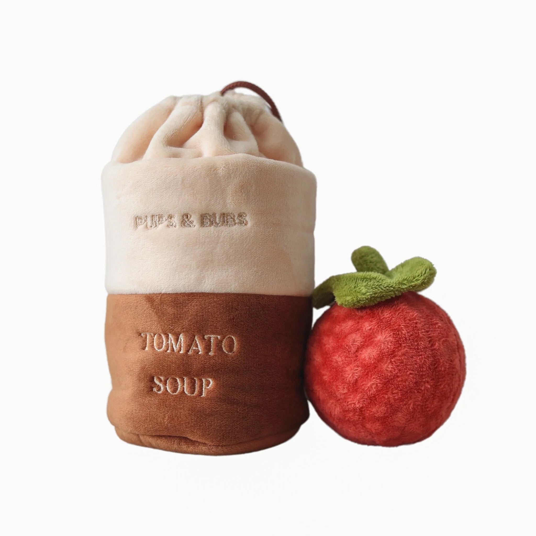 Clean studio shot on a white background showcasing the Pups and Bubs Tomato Soup interactive plush dog toy canister next to its round, red squeaky plush tomato.